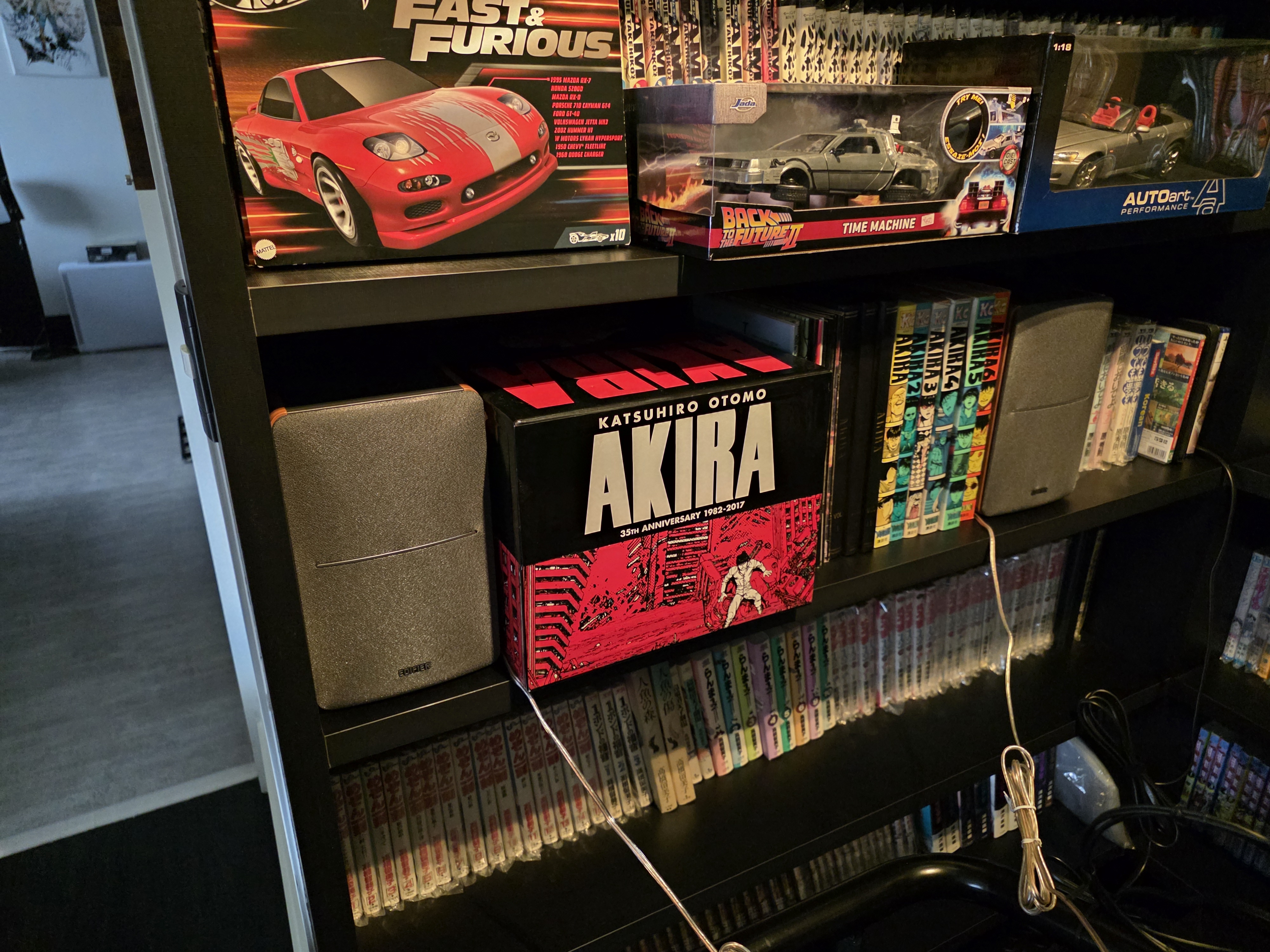 As Edifier P12 posicionadas nas estantes ao lado do cockpit, junto com a coleção de Akira e miniaturas de carros