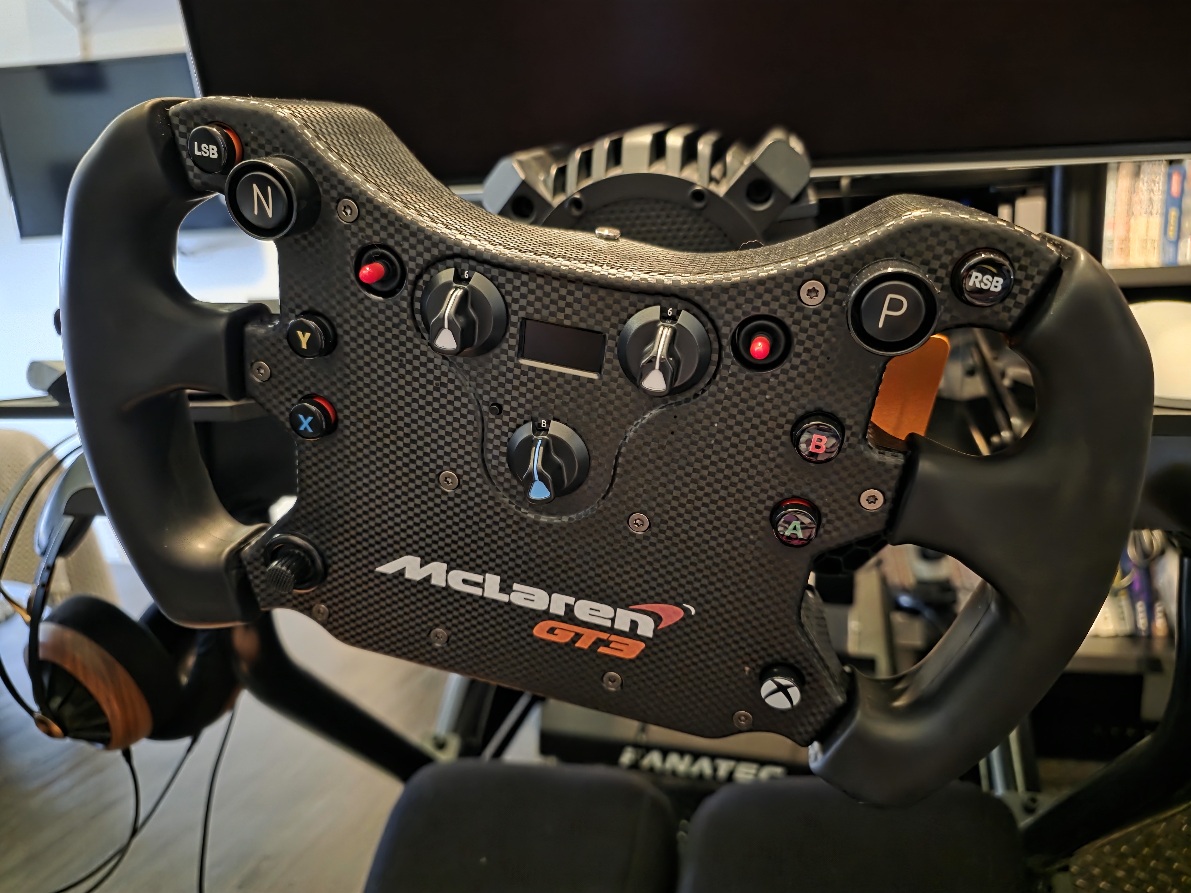 O volante McLaren GT3 V2 montado no cockpit — fibra de carbono e display OLED