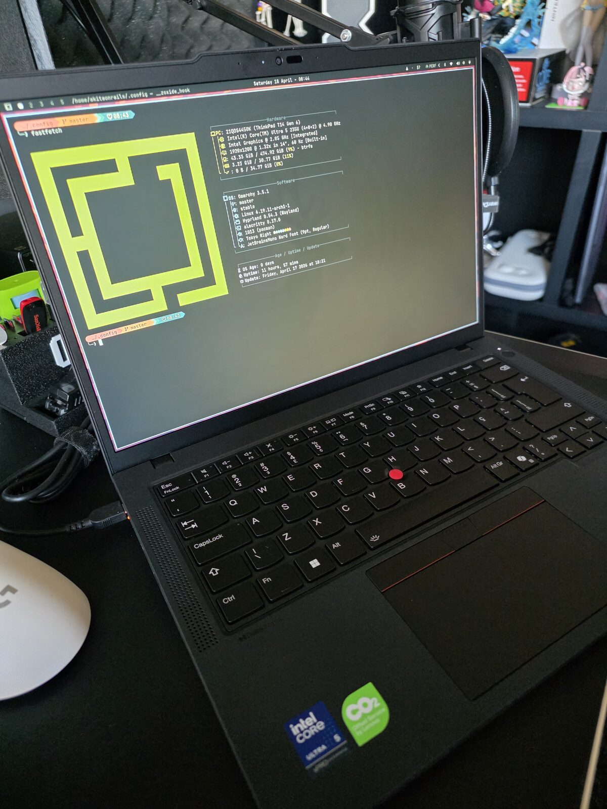 Thinkpad aberto numa bancada do escritório de impressão 3D, com fastfetch mostrando Omarchy no terminal